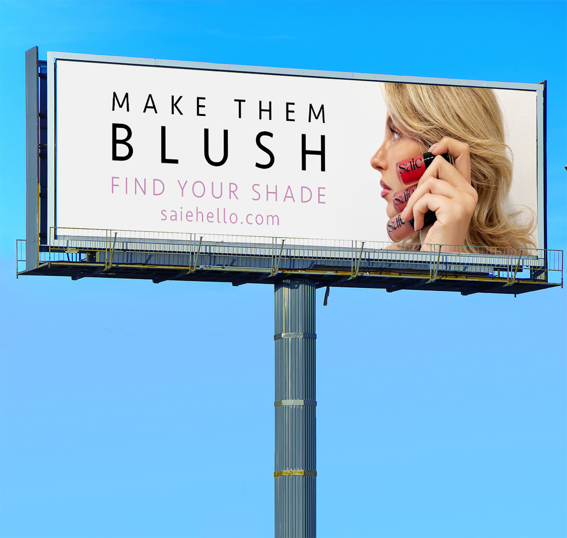 Find Your Shade billboard mockup showing a blonde model holding three Saie Dew Blush products, with Make Them Blush creative.